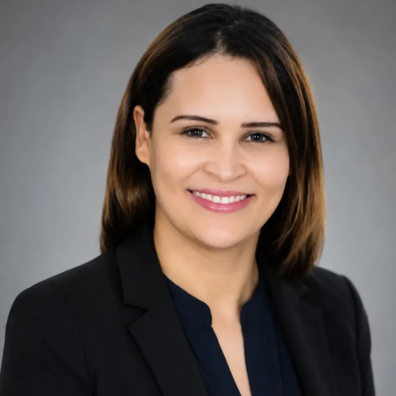 Ilhem Belkherchouche, dark hair to her shoulders, in a dark jacket against a grey background.